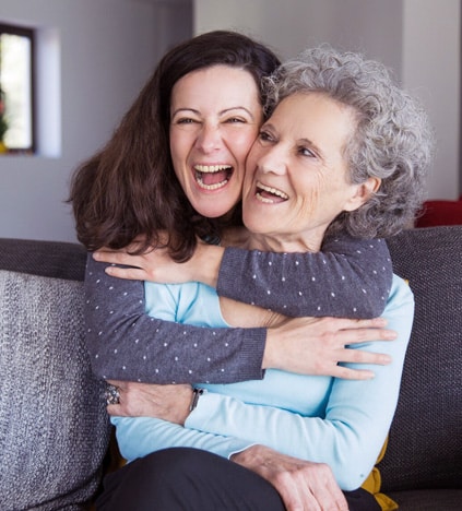 Two women smiling and hugging in a home interior setting.