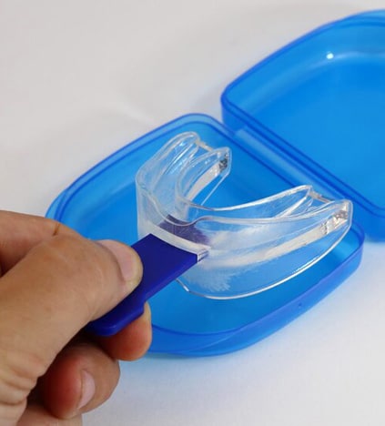 Clear teeth whitening trays held in hand over blue storage case