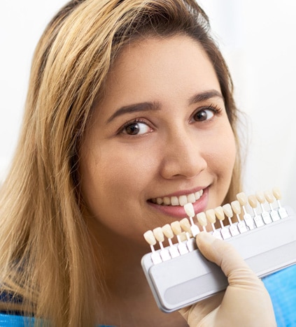 Young woman smiling while holding dental shade guide samples near her face.