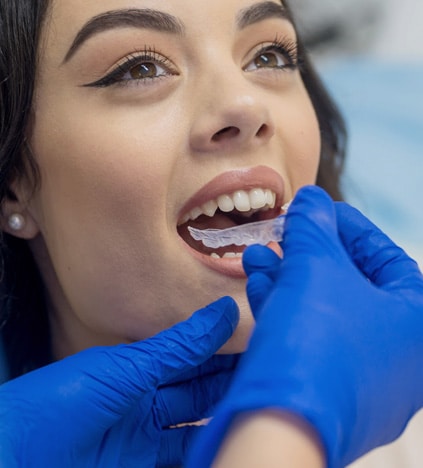 Dentist in blue gloves examining female patient's teeth during oral examination.
