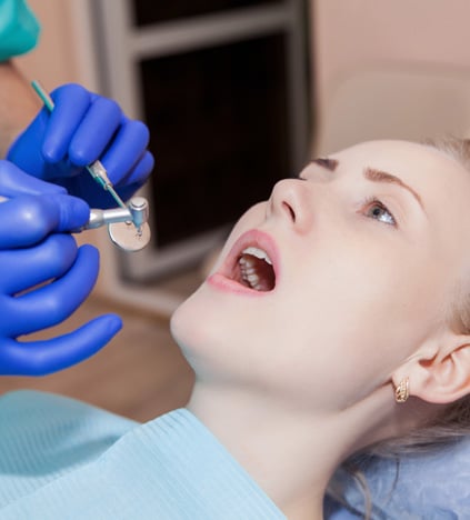 Child receiving dental examination with blue gloved dentist hand holding instrument in dental office.