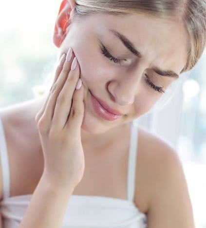 Woman touching her cheek in pain, suggesting dental discomfort or toothache.