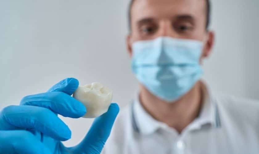 Dentist in blue gloves holding dental crown restoration model during consultation.
