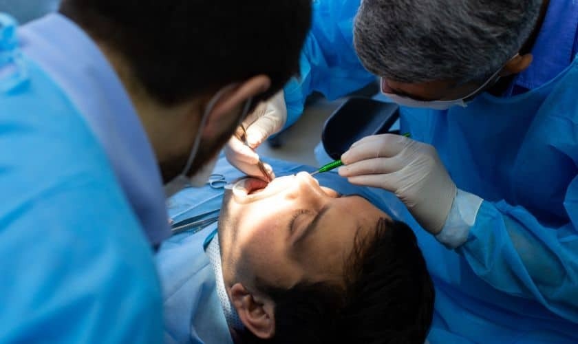 Oral surgeon performing dental implant procedure on patient in surgical setting.