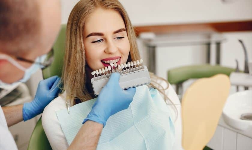 Dentist showing patient dental veneer shade guide to match natural tooth color during consultation.