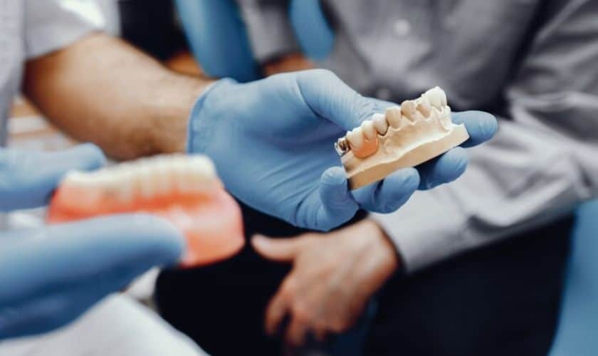 Dentist holding dental model showing teeth restoration options during patient consultation.